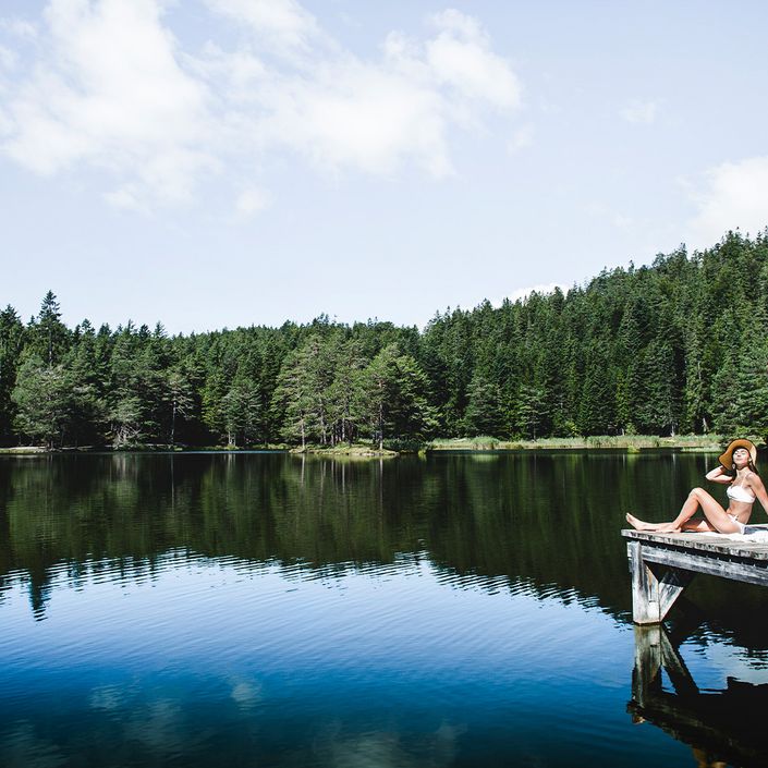 Frau sitzt am Holzsteg beim See